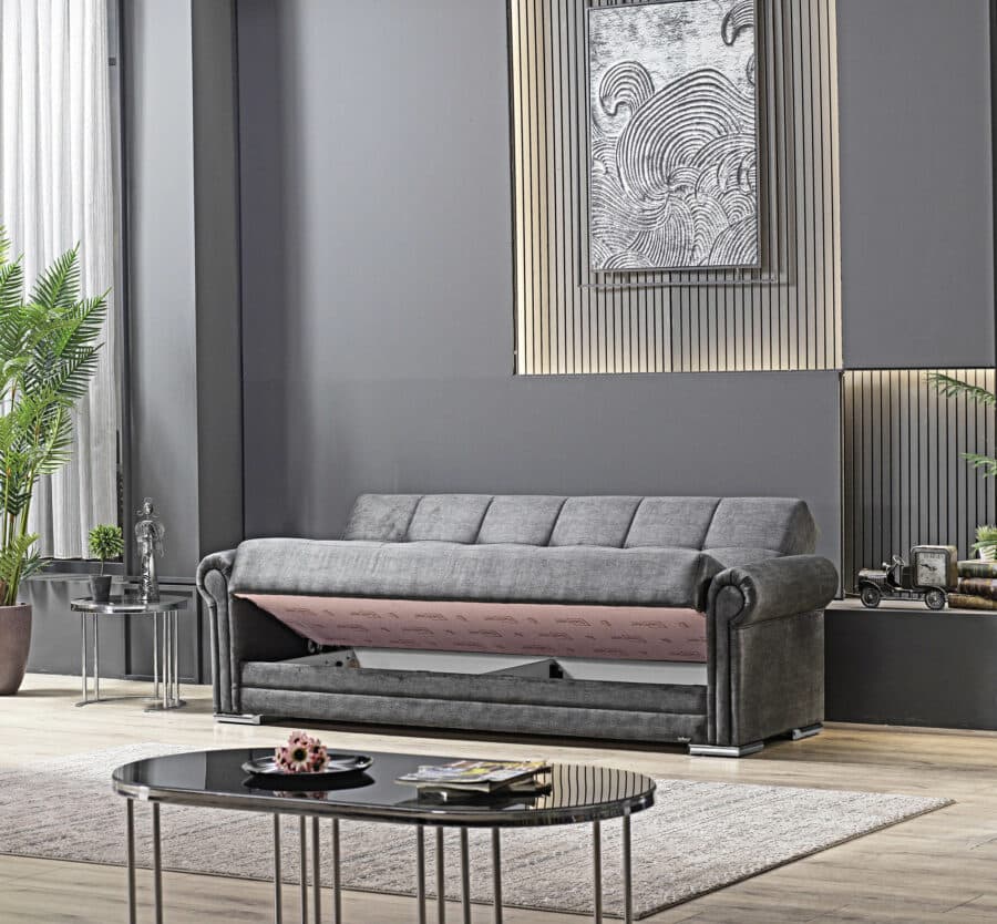 In einem modernen Wohnzimmer steht ein graues 3-Sitzer-Sofa 8500 Rosi von einem renommierten Möbelhaus vor einer dunklen Wand. Über dem Sofa hängt ein abstraktes schwarz-weißes Gemälde. Im Raum stehen eine Topfpflanze, eine kleine Statue und ein Couchtisch mit einem Dekoartikel darauf. Durch ein großes Fenster fällt Sonnenlicht in den Raum.